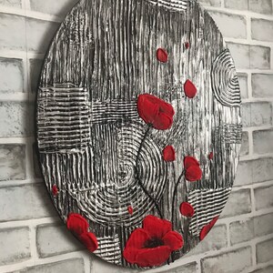 May include: Oval wall art with a textured black and silver background and vibrant red poppy flowers. The artwork features a mix of patterns, including vertical lines, squares, and circular designs, creating a striking contrast.