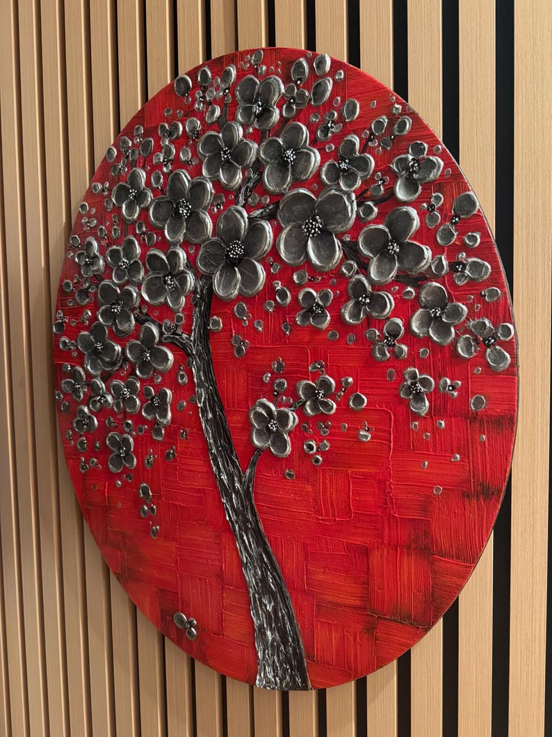 May include: A round canvas painting with a textured red background and a silver 3D tree with black flowers. The tree is in the center of the canvas and the flowers are blooming.