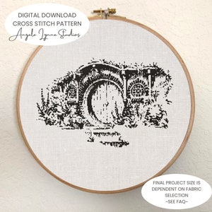 May include: Black and white cross stitch pattern of a hobbit hole with a round door. The pattern is framed in a wooden embroidery hoop. The text "DIGITAL DOWNLOAD CROSS STITCH PATTERN Angela Jynne Studios" is at the top of the image. The text "FINAL PROJECT SIZE IS DEPENDENT ON FABRIC SELECTION ~SEE FAQ~" is at the bottom of the image.