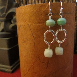 May include: A pair of silver earrings with green and white oval-shaped stones. The earrings have a hoop design and dangle from the ear.