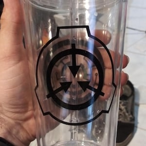 May include: A clear plastic tumbler with a black and white logo of a circle with an arrow pointing down and three arrows pointing out. The logo is a symbol of the SCP Foundation.