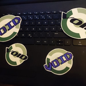 Peut inclure: Quatre autocollants avec un design circulaire vert et blanc. Le mot "VOID" est écrit en pixels en violet et bleu sur chaque autocollant. Le mot "OID" est écrit en noir sur un autocollant.