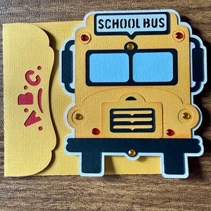 May include: A yellow school bus card with the words "SCHOOL BUS" on top. The card has a matching yellow envelope with the letters "A.B.C." cut out in red. The bus has blue windows and red and yellow accents.