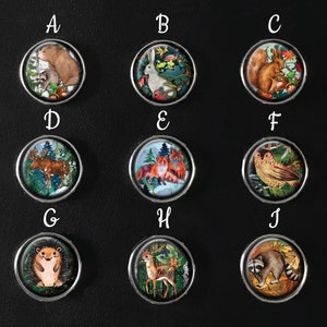May include: A collection of ten round, silver-rimmed magnets, each featuring a different woodland animal illustration. The designs include a bear, rabbit, squirrel, moose, foxes, owl, hedgehog, deer, and raccoon, set against colorful backgrounds.