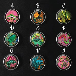 Puede incluir: Una colección de diez botones redondos con bordes plateados, cada uno con diseños coloridos de insectos y reptiles. Los botones presentan camaleones, escarabajos y otras criaturas en colores vibrantes como rosa, verde y naranja, sobre fondos estampados.