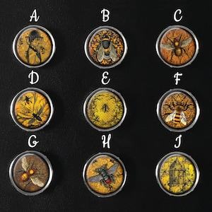 May include: Ten round, gold-colored metal buttons with different bee-themed designs. Each button has a letter label from A to J.