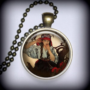 May include: A round glass pendant necklace with a vintage illustration of a woman in a red and white hat, a white blouse, and a black skirt. The woman is looking to the side and has her hand to her ear. The background is a brown and green forest scene.