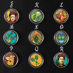 May include: A selection of circular magnets with silver edges, each displaying a vibrant Mexican-inspired design. The designs include Frida Kahlo, cocktails, hot sauce, Day of the Dead skulls, cacti, maracas, and musical instruments. The text "Cinco Mayo" is also present.