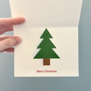 Pu&ograve; includere: Un biglietto bianco con un albero di Natale verde e il testo "Buon Natale" in rosso.