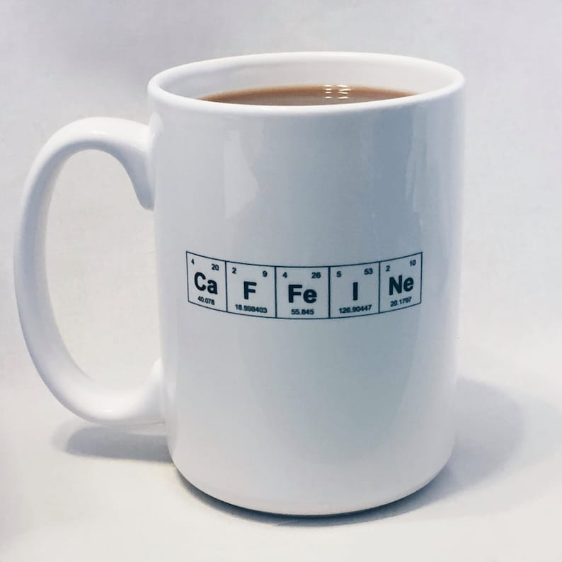 A white mug filled with coffee has Caffeine spelled out using the Periodic Table of the elements chemical symbols.