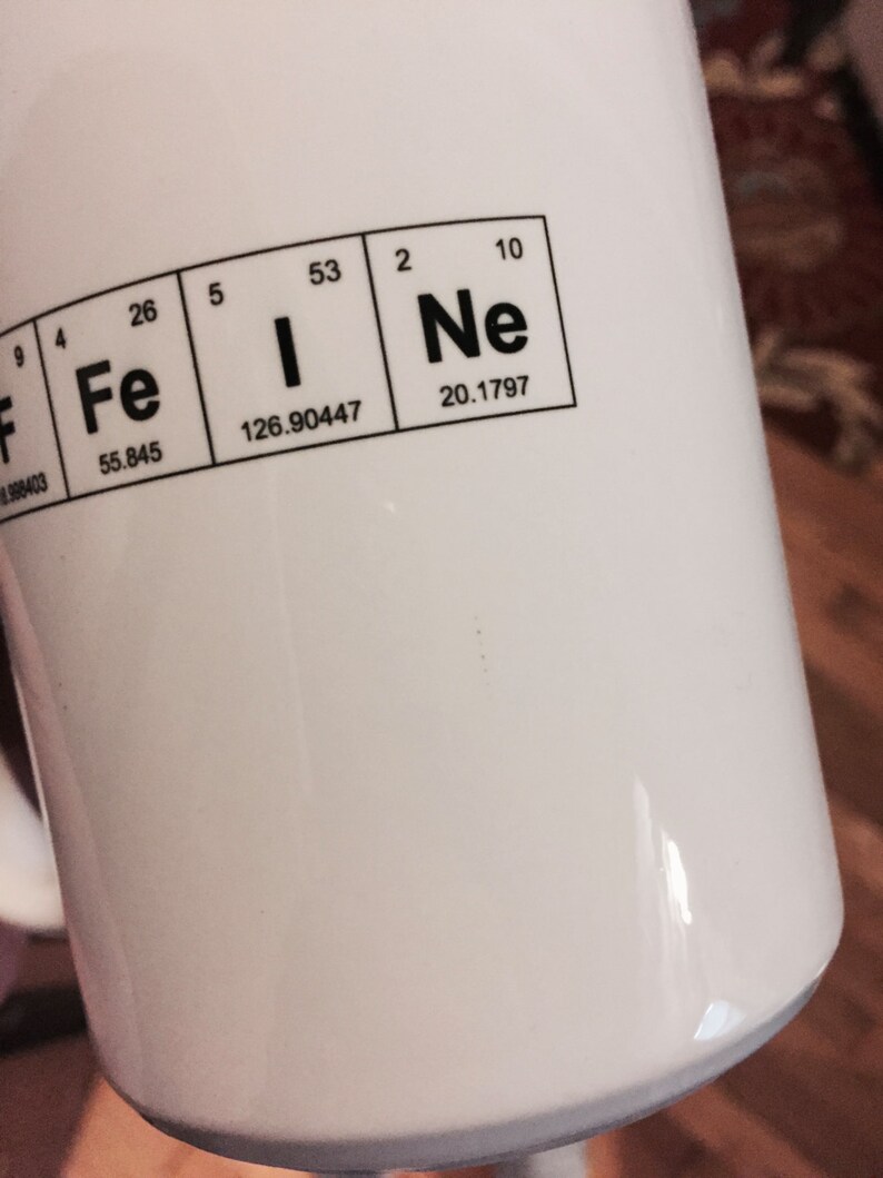 A detail image of a white mug with Caffeine spelled out using the Periodic Table of the elements. This image shows that the mug is an imperfect second as there are areas where ink appears outside of the bounds of the design.