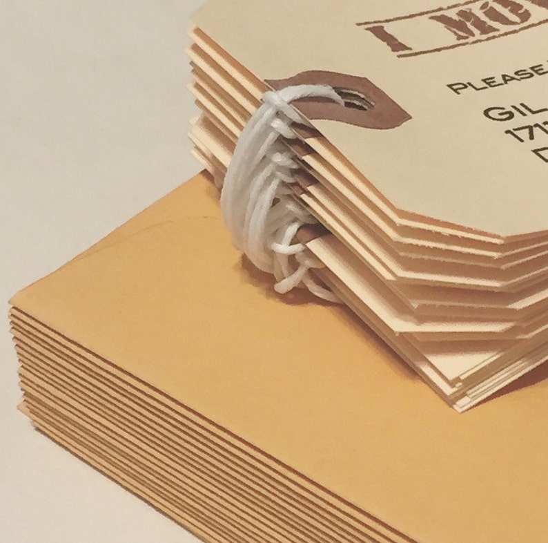 May include: A stack of brown envelopes with a stack of cream-colored tags tied together with white string. The tags have the text "I Must" and "Please" printed on them.