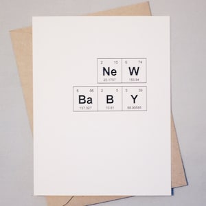 A white greeting card with the phrase “New Baby” spelled out using the Periodic Table of the elements. A Kraft envelope lays behind the card. The background is gray.