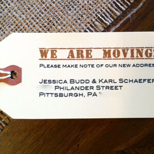 May include: A white tag with brown text announcing a move. The text reads "WE ARE MOVING! PLEASE MAKE NOTE OF OUR NEW ADDRESS: JESSICA BUDD & KARL SCHAEFER PHILANDER STREET PITTSBURGH, PA"