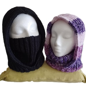 May include: Two knitted neck warmers, one black and one with purple and white stripes. The neck warmers are displayed on a green cushion.