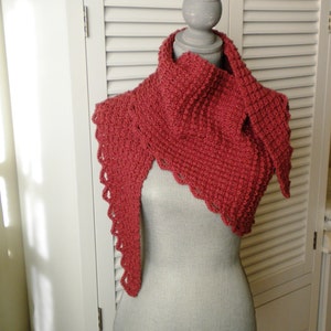 Puede incluir: Un chal de ganchillo rojo con un borde festoneado. El chal está drapeado sobre un maniquí.