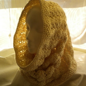 Pode incluir: Um cachecol de malha de cor creme com um padrão de tricô trançado. O cachecol está dobrado e drapeado sobre a cabeça de um manequim.