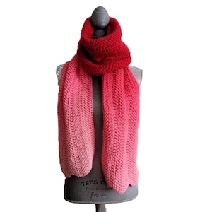 May include: A red and pink ombre knitted scarf with a chevron pattern. The scarf is displayed on a mannequin.