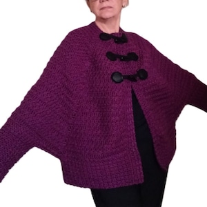 Puede incluir: Un cárdigan de punto morado con botones negros. El cárdigan tiene un corte holgado y mangas largas.