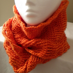Puede incluir: Un calentador de cuello de punto de color naranja brillante con un diseño retorcido. El calentador de cuello está hecho de hilo suave y es perfecto para mantenerse caliente en invierno.