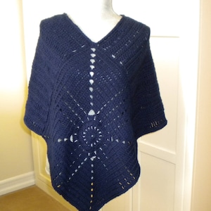 May include: A navy blue crocheted poncho with a diamond pattern and a circular design in the center.