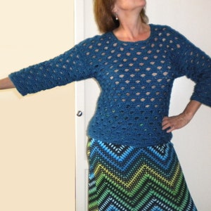 May include: A teal blue crocheted sweater with a lacy pattern. The sweater has a round neckline and three-quarter sleeves.