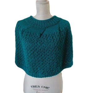 May include: Teal knitted poncho with a delicate openwork pattern. The poncho is displayed on a mannequin.