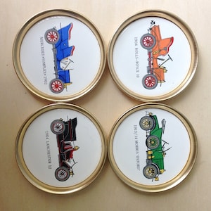 May include: Four round coasters with gold trim, each featuring a vintage car illustration and the year and make of the car. The cars are a 1904 Rolls-Royce 10, a 1913/14 Morris 'Oxford', a Mercedes Simplex 1902, and a 1904 Lanchester 12.