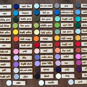 Op de afbeelding: Een kaart met 60 kleurstalen met namen voor elke kleur. De kleuren zijn gerangschikt in rijen en kolommen op een houten achtergrond.
