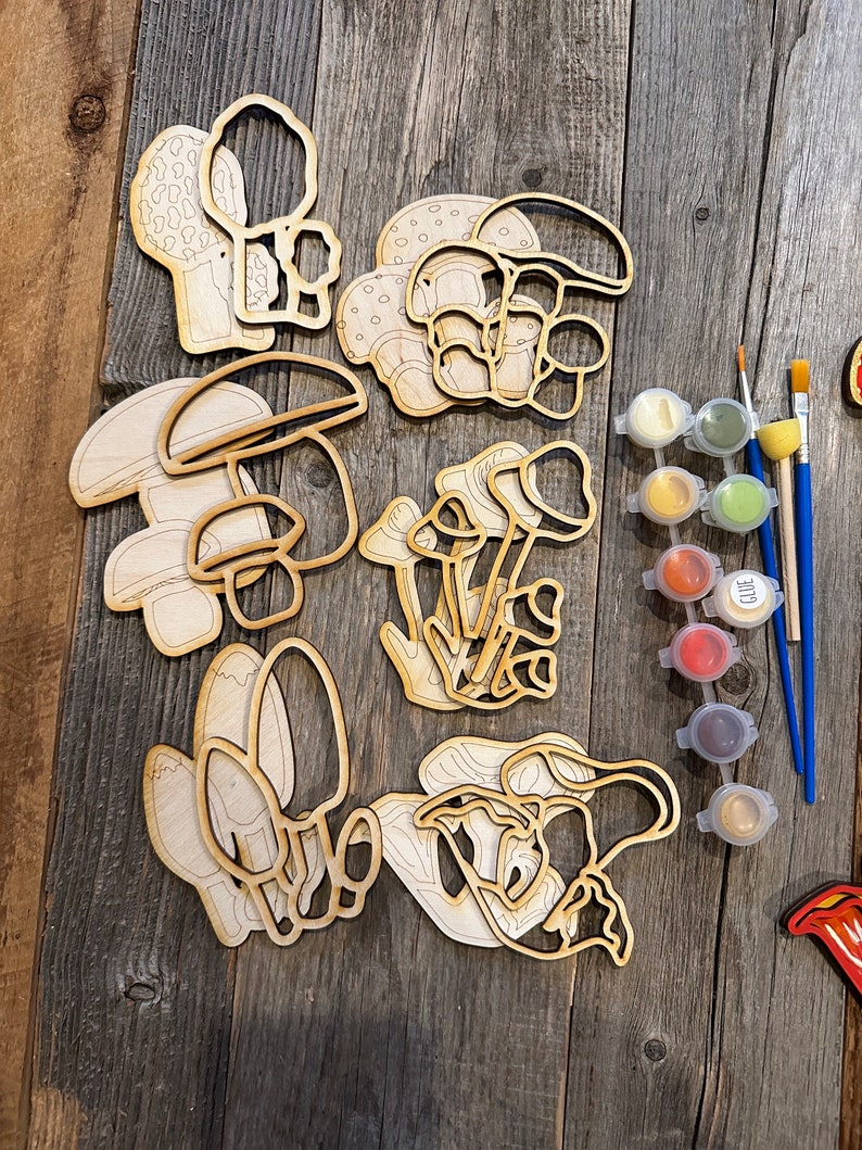 Op de afbeelding: Een set houten paddenstoelvormen om te beschilderen, in verschillende maten en stijlen. De set bevat verfpotjes in verschillende kleuren, kwasten en een lijmstok.