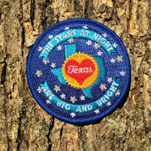 May include: Blue embroidered patch with a white star outline and the text "The Stars At Night Are Big And Bright" around a turquoise outline of the state of Texas with a red heart in the center that says "Texas".