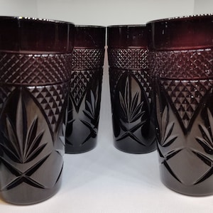 May include: Four ruby-colored, cut-glass tumblers. Each glass features a diamond pattern near the rim and a stylized leaf design. The glasses are cylindrical and have a classic, elegant appearance.