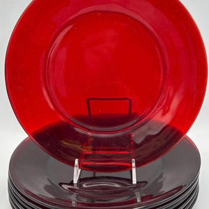 May include: A set of six red glass dinner plates. The plates are a vibrant red color and have a simple, classic design. The plates are stacked on top of each other, with one plate displayed on a clear stand.