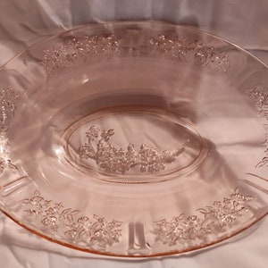 May include: A pink oval serving dish with embossed floral designs. The dish features a central floral arrangement and additional floral patterns around the rim. The glass dish is a soft pink colour.