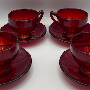 Peut inclure: Un ensemble de quatre tasses à thé et soucoupes assorties en verre rouge rubis. Chaque tasse présente un bol arrondi avec une anse incurvée et une base sur pied. Les soucoupes ont un bord festonné. Le verre est translucide et rouge.