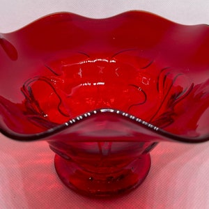 May include: A striking red glass bowl with a frilled edge and a pedestal base. The bowl has a glossy finish and etched floral patterns. The rim is decorated with small white dots. A decorative item for serving or display.