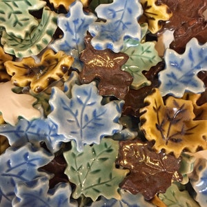 May include: A collection of ceramic leaf tiles in various shades of blue, green, brown, and yellow. The leaves are all different shapes and sizes, and some have a raised design.