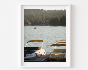 May include: Two white boats with yellow canopies are docked at a lake. The boats are facing the camera. The lake is calm and the water is reflecting the sky. In the distance, a small red boat is on the water.