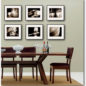 Op de afbeelding: Een eettafel met zes stoelen, gedekt met een witte kom en glazen. De muur achter de tafel is versierd met zes zwart ingelijste foto's van wijn, druiven en vaten.
