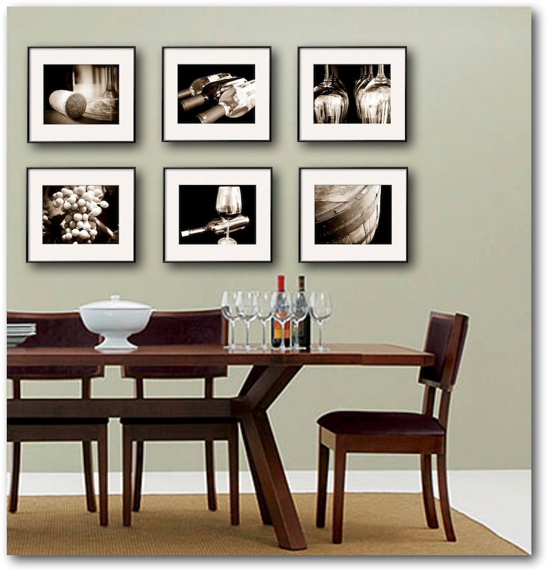 Op de afbeelding: Een eettafel met zes stoelen, gedekt met een witte kom en glazen. De muur achter de tafel is versierd met zes zwart ingelijste foto's van wijn, druiven en vaten.