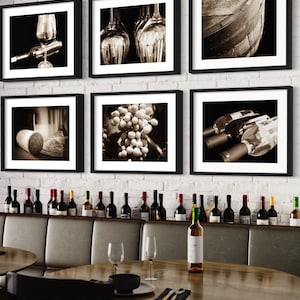 Op de afbeelding: Een set van zes ingelijste zwart-witfoto's die verschillende wijn-gerelateerde afbeeldingen tonen, waaronder druiven, wijnflessen, glazen en een houten vat. De foto's worden weergegeven op een witte bakstenen muur boven een houten tafel met wijnflessen en glazen.
