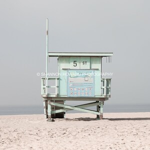 May include: A light blue lifeguard stand with a white sign that reads "5th St. Ocean Safety Patrol" on a sandy beach.