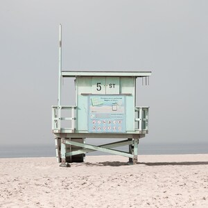May include: A light blue lifeguard stand on a sandy beach with the text "5 ST" on the front. The stand has a white sign with black text and symbols.