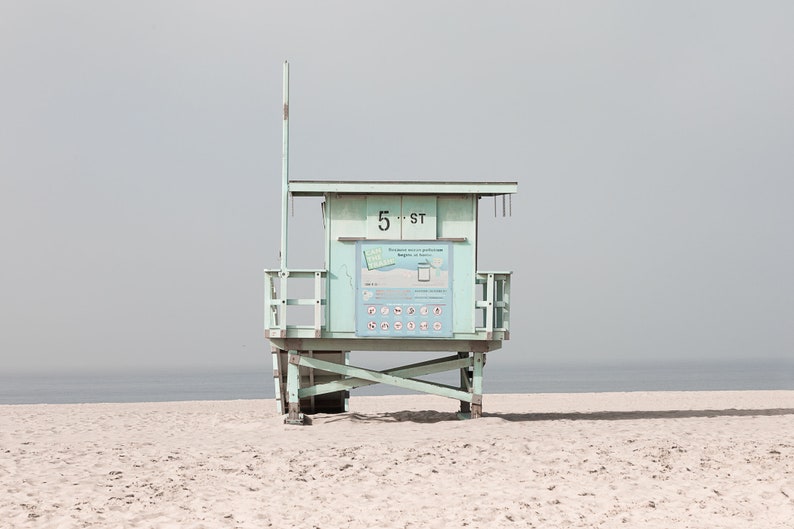May include: A light blue lifeguard stand on a sandy beach with the text "5 ST" on the front. The stand has a white sign with black text and symbols.