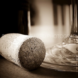 Op de afbeelding: Een close-up van een kurk van een wijnfles, met een getextureerd oppervlak. De kurk ligt op een houten oppervlak naast een helder glazen wijnglas.