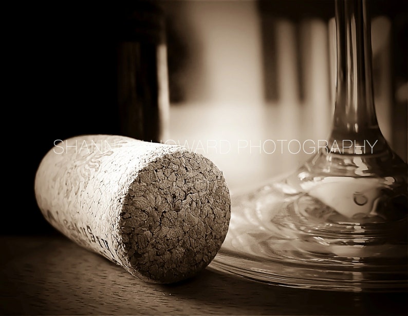 Op de afbeelding: Een close-up van een kurk van een wijnfles, met een getextureerd oppervlak. De kurk ligt op een houten oppervlak naast een helder glazen wijnglas.