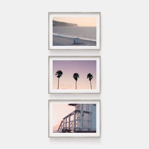 May include: Three framed photographs of a beach scene. The top photo shows a lifeguard stand on a sandy beach with the ocean in the background. The middle photo shows three palm trees silhouetted against a purple sky. The bottom photo shows a close-up of a lifeguard stand with a wooden staircase.