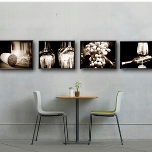 Op de afbeelding: Zes zwart ingelijste sepia-kleurige foto's van wijn gerelateerde items die aan een muur hangen boven een kleine ronde tafel met twee stoelen. De foto's bevatten een wijnvat, een kurk, wijnflessen, druiven, een wijnglas en wijnflessen.