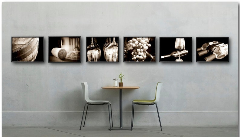 Op de afbeelding: Zes zwart ingelijste sepia-kleurige foto's van wijn gerelateerde items die aan een muur hangen boven een kleine ronde tafel met twee stoelen. De foto's bevatten een wijnvat, een kurk, wijnflessen, druiven, een wijnglas en wijnflessen.