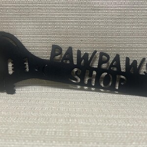 May include: Black metal wrench shaped sign with the words "Paw Paws Shop" cut out.